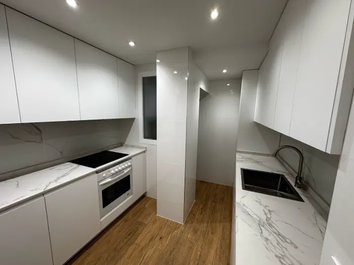 Cocina blanca sin tiradores con encimera y frontal efecto mármol y suelo de madera